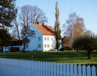TO etasjes hus og stakittgjerde rundt