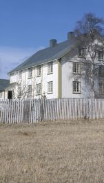 To etasjes hvitmalt hus med åker og stakittgjerde foran