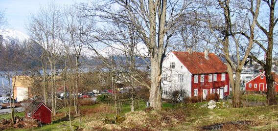 to etasjes trehus med en side som er rødmalt og den andre som er hvitmalt ligger i helling med fjell i bakgrunn