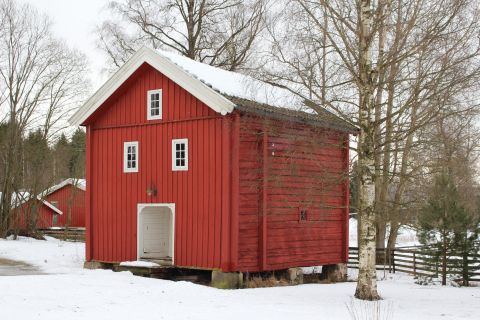 Rødt stabbur med sne på taket og på bakken.