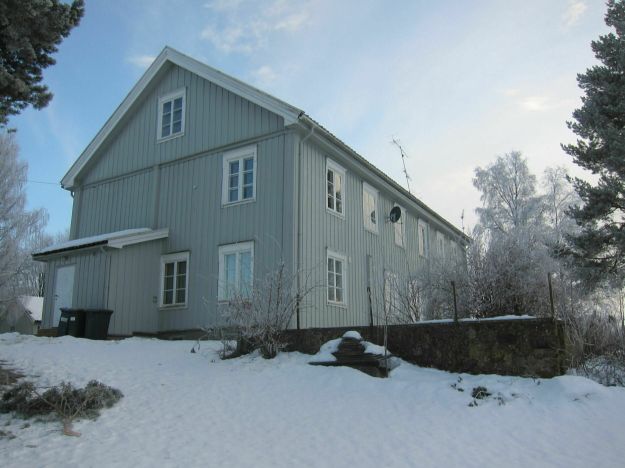 Hvitt trehus på to etasjer. Våler prestegård sett fra gavlssiden i vinterlandskap.