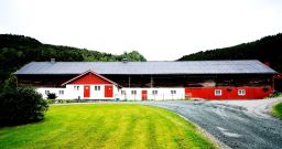 Rødmalt driftsbygning med plen i forgrunnen
