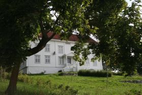 Storslått hvitmalt bygning med hage i forgrunnen