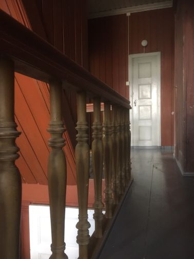 Smal lang gang med gelender på venstre side som leder til dør i enden