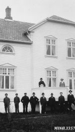 sort hvitt bilde av prestegården med dresskledde menn foran fasaden