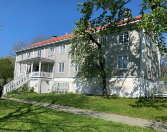 Stort gråhvitt hus i to etasjer med gressplen foran