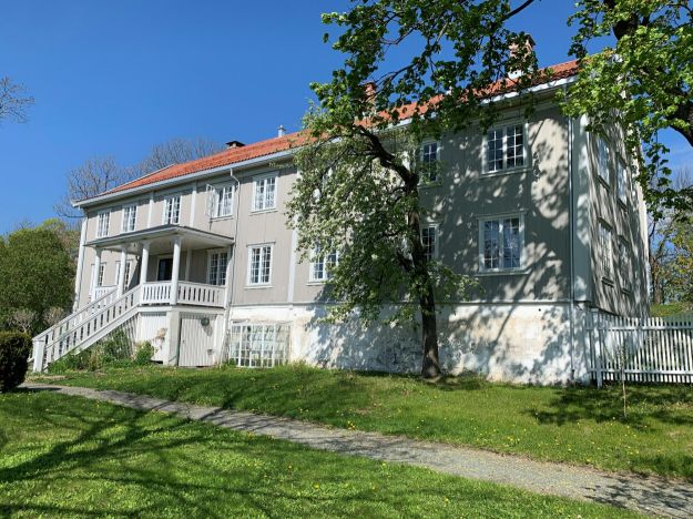 Stort gråhvitt hus i to etasjer med gressplen foran