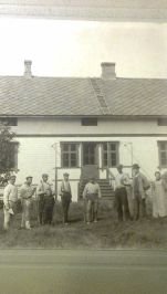 Sort hvitt gammelt bilde der mange arbeidsfolk er avfotografert  foran huset .