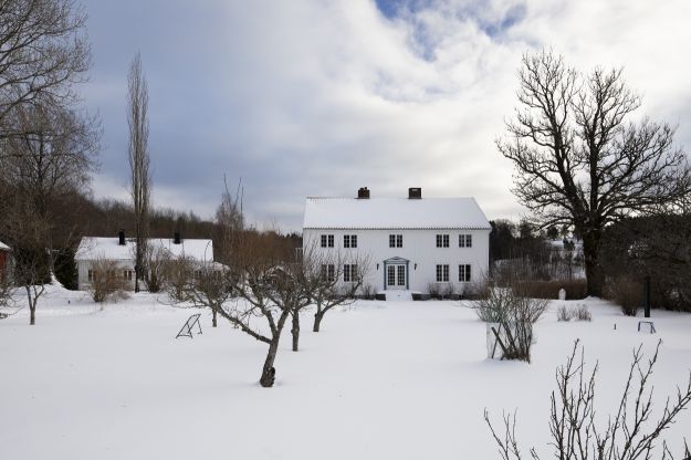 Hvit trehus midt på vinteren med snø på plenen foran huset