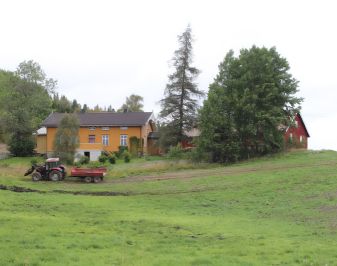 grønn plen med okergult hus og rød traktor i bakgrunn