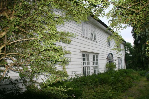 Hvitt trehus med trær foran fasaden