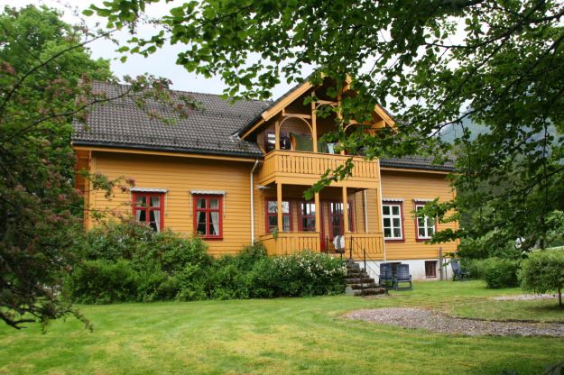 Okergult hus, trær og gressplen