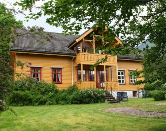 Okergult hus, trær og gressplen