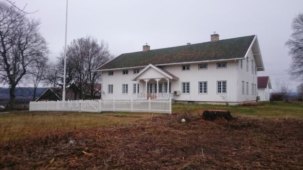 lang trehusbygning med stakittgjerde og flaggstang