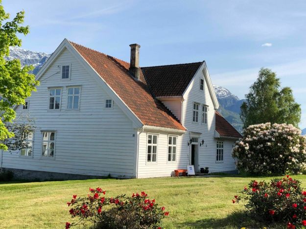 Hvitt trehus omgitt av gress og blomsterbusker