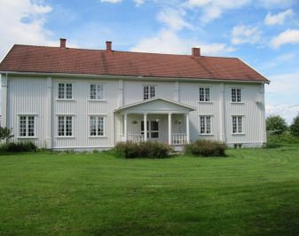 Stor hvit trebygning med gressplen foran