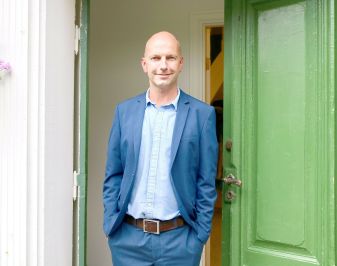 Mann i blå dress står i inngangen til Luster prestegård