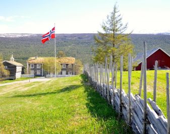 Foto av Lesja prestegård med gressbakke med flaggstang i forgrunnen