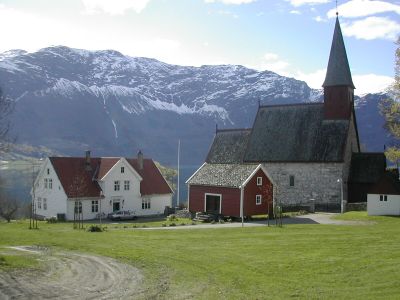 Hus og kirke omgitt av fjell og grønn mar