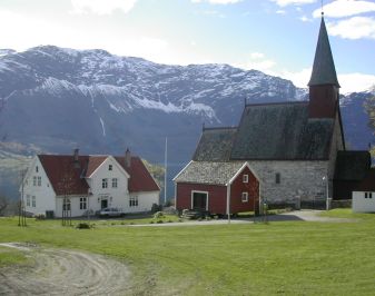 Hus og kirke omgitt av fjell og grønn mar