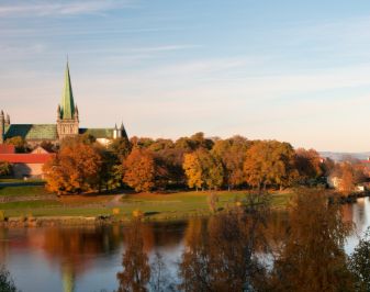 Autumn inOversiktsbilde viser Nidarosdomen omgitt av trær med høstfarger. I forgrunnen renner Nidelva.