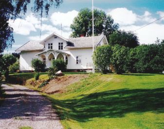 Hvitt våningshus med oppkjøring, hage og flaggstang