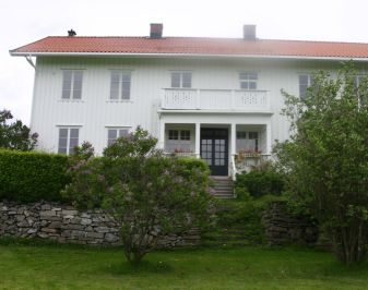 Hvitt, stort hus med hage, mur og hekk i forgrunnen