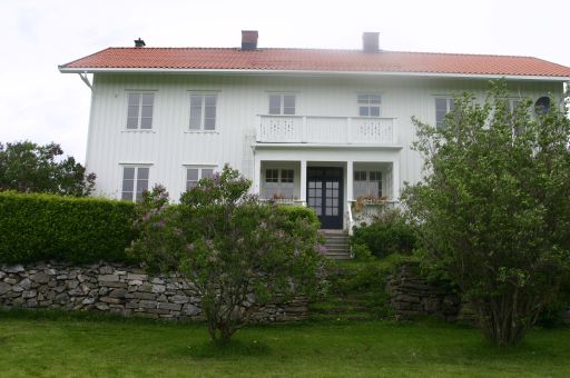 Hvitt, stort hus med hage, mur og hekk i forgrunnen