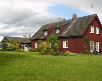 Nyere rødmalt trehus med stor hage i forkant.