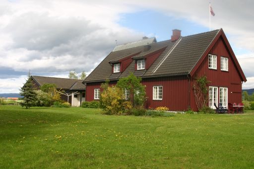 Nyere rødmalt trehus med stor hage i forkant.