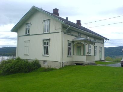 Hvitmalt tømmerhus med hage og tun i forkant