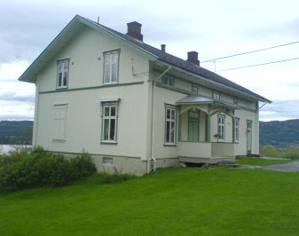 Hvitmalt tømmerhus med hage og tun i forkant