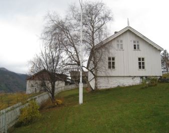 Hvitt våningshus med trær og stakittgjerde i forgrunnen