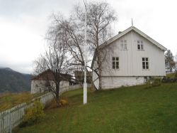 Hvitt våningshus med trær og stakittgjerde i forgrunnen