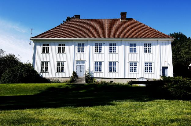 Storslått hvit trebygning med parkmessig hage