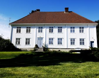 Storslått hvit trebygning med parkmessig hage