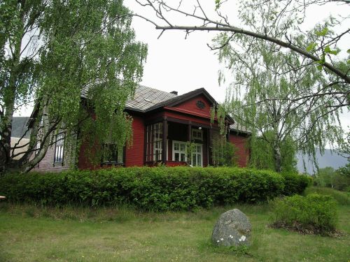 Rødmalt trehus med hekk og hage i forgrunnen