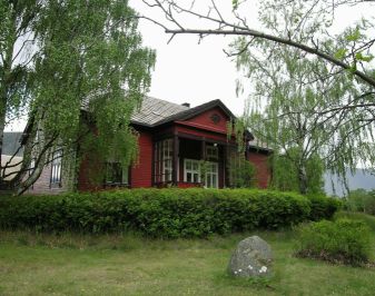 Rødmalt trehus med hekk og hage i forgrunnen