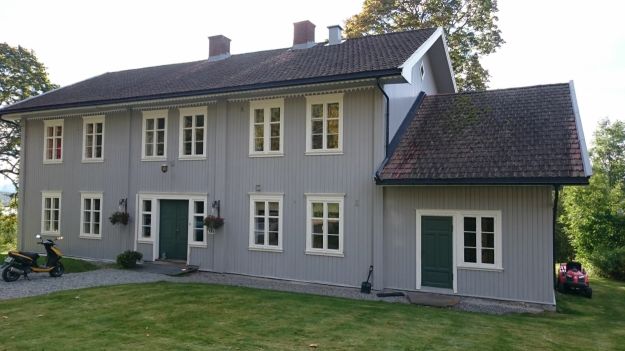 Gråmalt trehus i to etasjer. Hagen i forgrunnen
