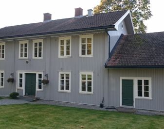 Gråmalt trehus i to etasjer. Hagen i forgrunnen