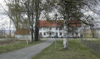 Flott, hvit trebygning med tuntre og alle inn til tunet