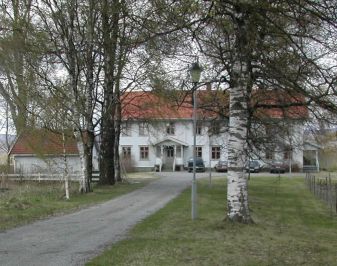 Flott, hvit trebygning med tuntre og alle inn til tunet