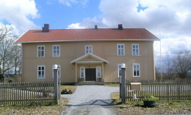 Gulmalt trebygning med stakittgjerde og tun i forgrunnen