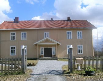 Gulmalt trebygning med stakittgjerde og tun i forgrunnen