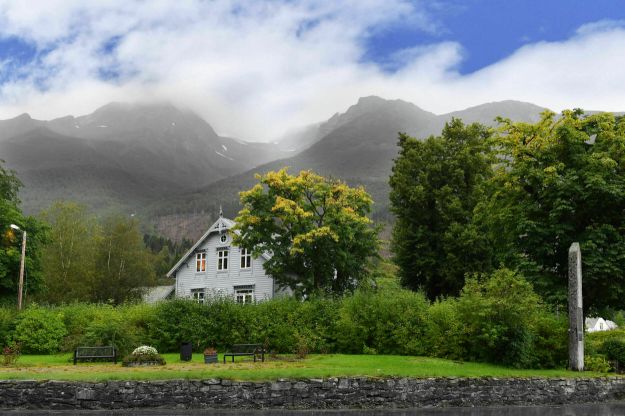 Søbø prestegard i Møre. Trehus omgitt av grønne trær og fjell. Foto