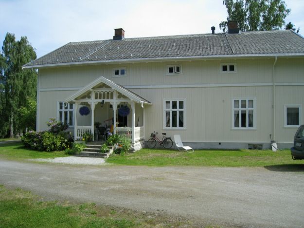 Hvitmalt stort trehus med tunet i forkant