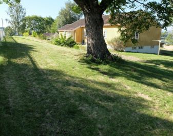 Nyere gulmalt bolig med tuntre og hage i forgrunnen