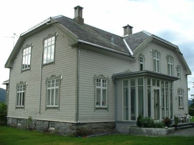 Hus med halvvalmet tak og veranda med smale glassvinduer.