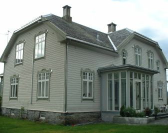 Hus med halvvalmet tak og veranda med smale glassvinduer.