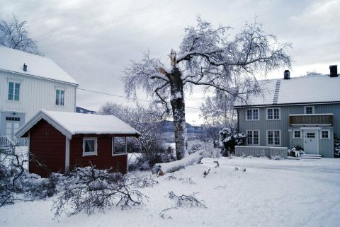 To-etasjes tømmerbygning fra attenhundretallet og en rød bygning om vinteren med snø.